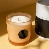 yellow background with a candle with slight orange tinted candle tin and a black circle on it. "earth" scented candle