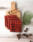 Four Diamond Cocktail Napkins in Ruby on a Serving Board with Pinecones surrounding and Green glasses to the right
