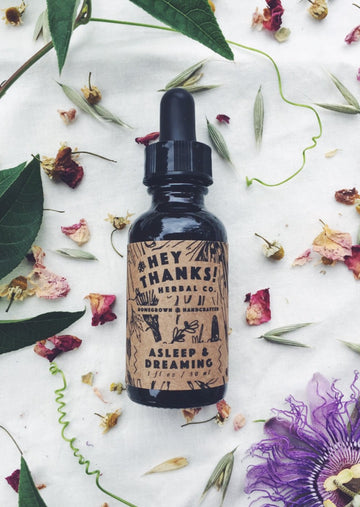 Photo of a dropper bottle laying flat with a tan sleeve saying "Hey thanks! Herbal Co. Homegrown & Handcrafted. Asleep and Dreaming 1 ft oz / 30 ml" Around the bottle are dried roses, leaves and other flowers